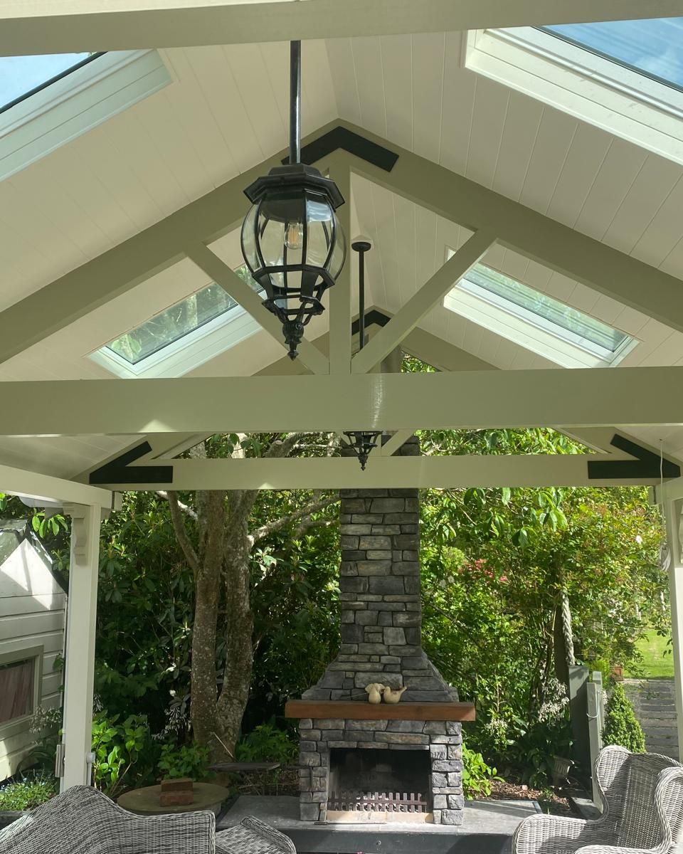 Covered outdoor patio built by Edify, with exposed trusses, skylights, a hanging lantern and a stone fireplace
