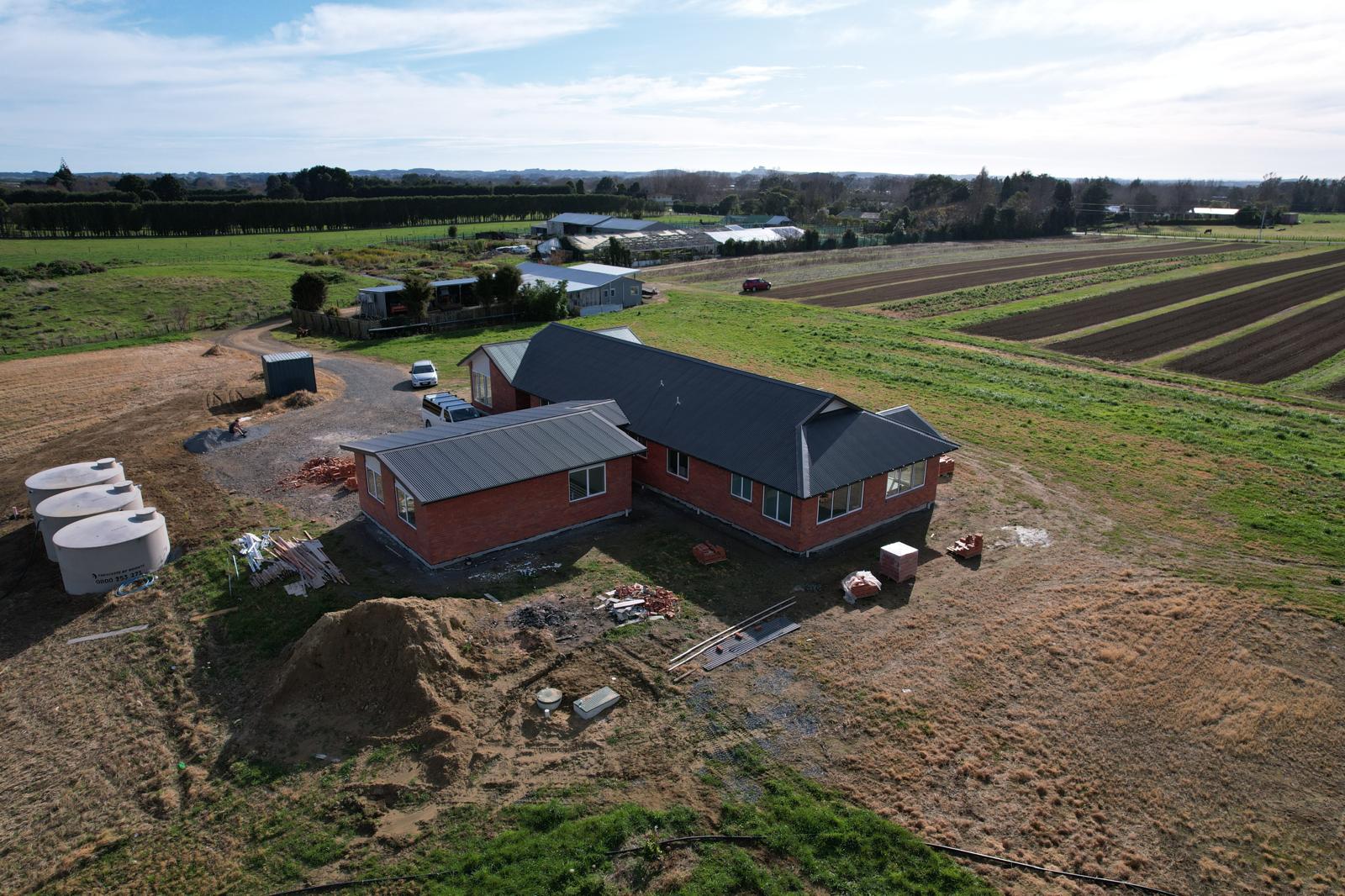 Aerial view of a finished brick family home and large garage on a farm in Ohau