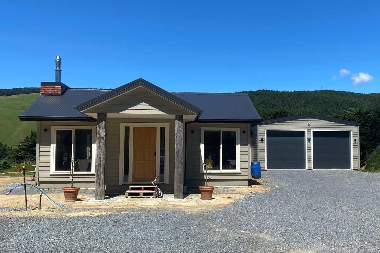 A completed Edify new build: weatherboard home with timber front door, covered entrance and double garage, set against green Wellington hills