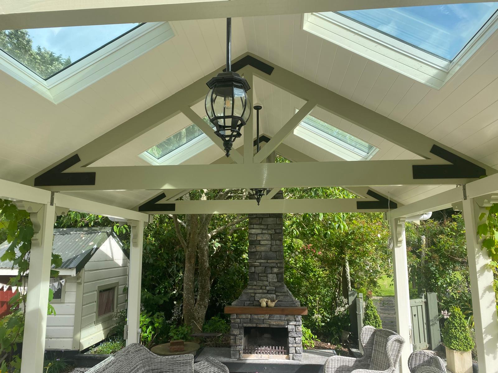 Covered outdoor patio with a peaked roof, skylights, stone fireplace and seating area